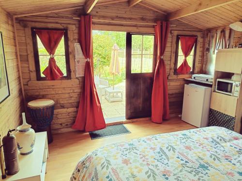 a bedroom with a bed and a kitchen with red curtains at Chalet dans notre jardin in Parigné