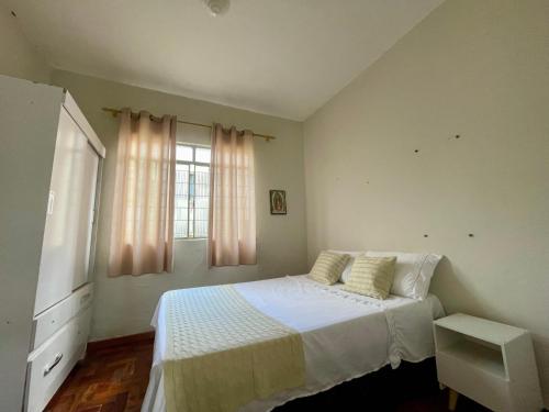 a bedroom with a bed with white sheets and a window at Casa Jardim Centro in Patos de Minas