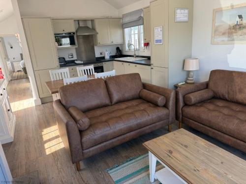 a living room with two brown couches and a kitchen at Sandy Bay Hideaway - Part of the The Bay Filey Holiday Village with pool, gym and direct beach access, pub, restaurant, tennis and meadows walks in Filey