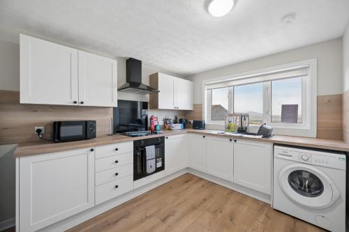 a kitchen with white cabinets and a washer and dryer at Lime Grove House in Dalkeith