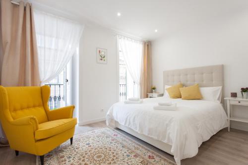 a white bedroom with a bed and a yellow chair at White Tiles in City Center in Lisbon