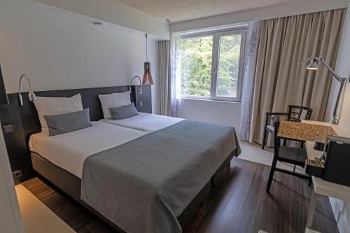a bedroom with a bed and a desk and a window at Hotel Landgoed Zonheuvel in Doorn