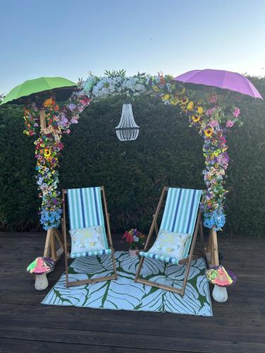 two chairs sitting under an arch with flowers and an umbrella at Beautiful Rural Holiday Chalet With Hot tub and Igloo cinema in Lincolnshire