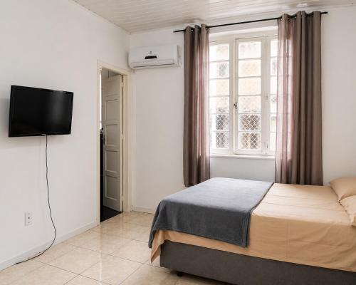 a bedroom with a bed and a tv and a window at Hostel & Coffe Bahia in Porto Alegre