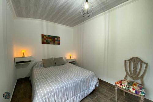 a white bedroom with a bed and a chair at SH Aparts Depto 1 in Coronel Suárez