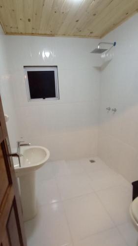 a white bathroom with a sink and a tv on the wall at Chalé dos ventos in Itamonte