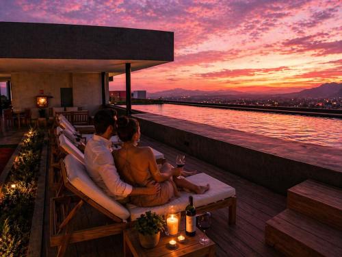 a couple sitting in chairs on a balcony watching the sunset at Apto Deluxe, 3 hab, piscina y rooftop en Escalón in San Salvador