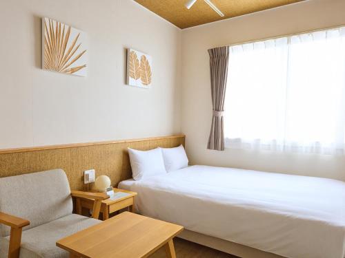 a hotel room with a bed and a chair and a window at Ishigakijima Hotel Cucule in Ishigaki Island