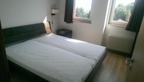 a bed in a bedroom with two windows at Galerius Golden Beach Apartment in Siófok