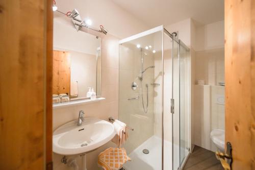a white bathroom with a sink and a shower at Hotel Rochushof in Schenna