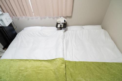 a bed with white sheets and a green blanket at Ijiri Relax stay in Fukuoka