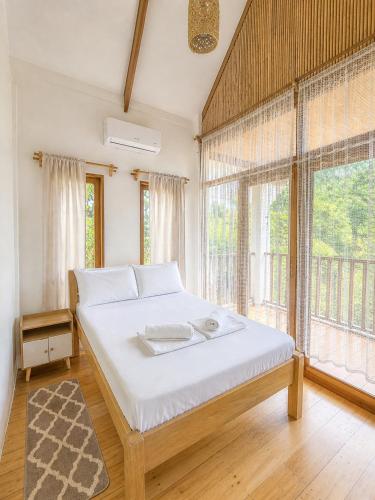 a bedroom with a bed with white sheets and windows at MHARI Bungalows and Rooms in Tubod