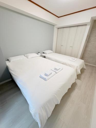 two beds in a room with white walls and wood floors at カリエンテ三宮202 in Kobe