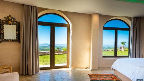 a bedroom with three windows and a bed with a view at Bhalil Farm House in Sefrou