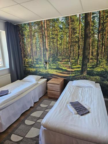 two beds in a room with a mural of a forest at Hotell Hemgården in Bengtsfors