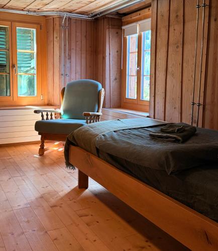 a bedroom with a bed and a chair and windows at Blüemlisalp-Huus im Kiental in Kiental