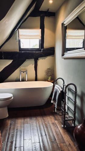 a bathroom with a white bath tub and two windows at Cottage in the Hambleden Valley in Henley on Thames
