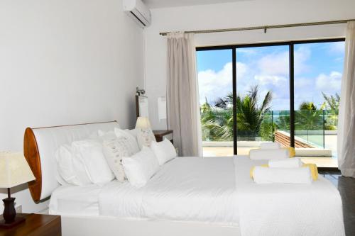 a bedroom with a white bed and a large window at Beach Penthouse BELMARE in Belle Mare