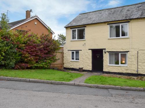 a yellow house with a black door on a street at Richmond Cottage in Ashby Saint Ledgers