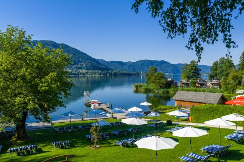 Eine Gruppe von Tischen und Sonnenschirmen neben einem See in der Unterkunft Seehotel Hoffmann in Steindorf am Ossiacher See