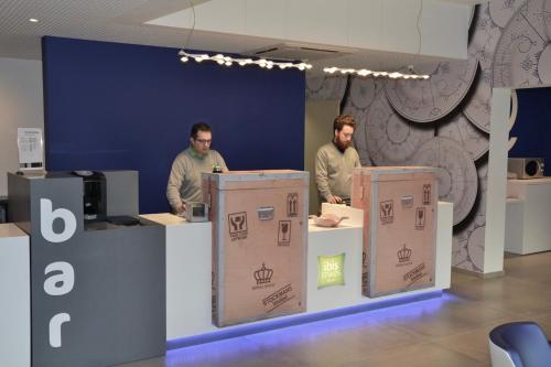 two men standing in a room with boxes at Ibis Styles La Louvière in La Louvière
