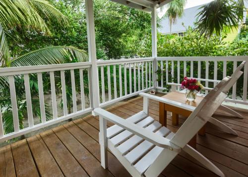 a white rocking chair on a porch with a wooden table at Weezie's Ocean Front Hotel and Garden Cottages in Caye Caulker