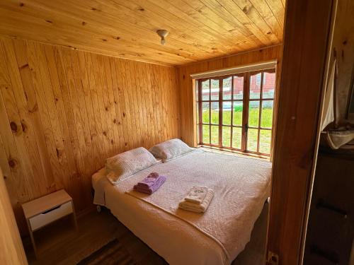 a small bed in a wooden room with a window at Cabañas Alelí in Chaitén