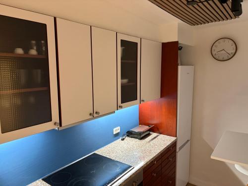 a kitchen with white cabinets and a clock on the wall at Lille Skovgaarden ved parken med gratis parkering in Randers