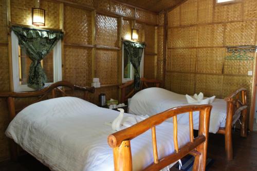 two beds in a room with wooden walls and windows at Soe Ko Ko Beach House & Restaurant in Ngwesaung