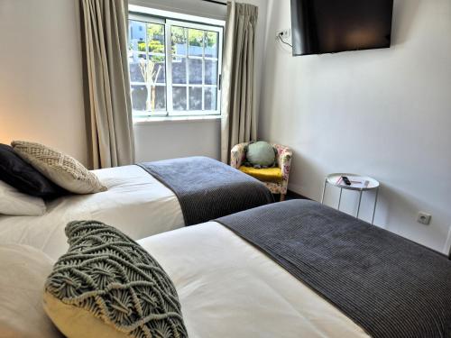 two beds in a room with a window and a chair at Cimo das Dutras in Horta