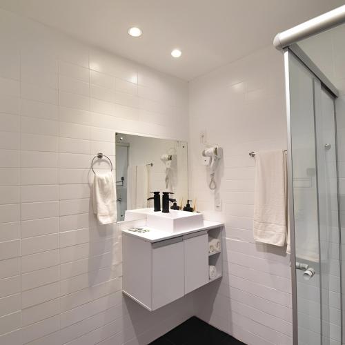 a white bathroom with a sink and a shower at Metropolitan Flats in Curitiba