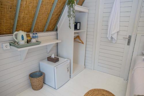 a white bathroom with a small refrigerator and a door at D'Yuki Huts Lembongan in Nusa Lembongan