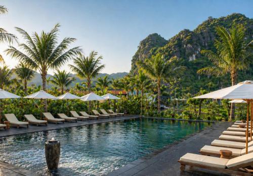 a pool with chairs and umbrellas and palm trees at Aman Retreat Ninh Binh in Ninh Binh