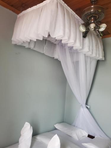 a bedroom with a ceiling fan and white curtains at Torchys in Kisumu