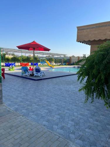 a patio with an umbrella and chairs and a pool at Villa Layan الريف الاوروبي in Madīnat as Sādāt