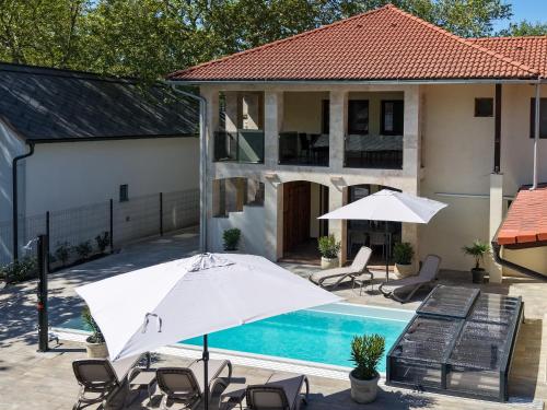 a pool with chairs and an umbrella next to a house at Mirage Apartments & Pool - Balatonboglar in Balatonboglár