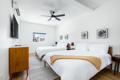 two beds in a room with white walls and a ceiling fan at NEWGamesTVsHeated PoolFirepitFireplace in Coachella