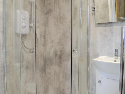 a shower with a glass door next to a sink at Angerton Cottage in Carlisle