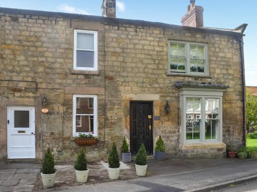 an old stone house with potted trees in front of it at Bailey Cottage in Staindrop