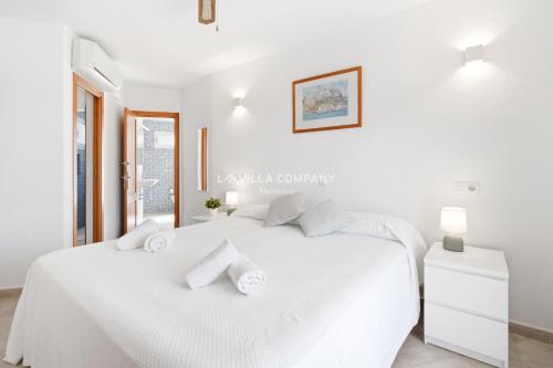 a white bedroom with a white bed and a window at Villa FLEUR in Cala en Porter