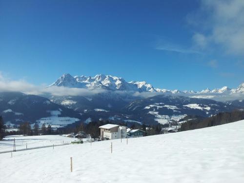 a snow covered mountain with a house in the foreground at Zistelberghof in Werfenweng