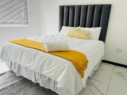 a bedroom with a large bed with white sheets and yellow blanket at Oregano Estate in Swakopmund