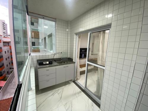 a white tiled bathroom with a sink and a shower at Atlântico 33 Guilhermina in Praia Grande