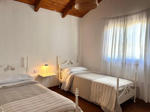 a white bedroom with two beds and a window at Cabaña Cali in Cafayate