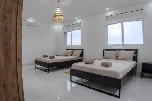 two beds in a white room with two windows at Villa Raha in Selouane