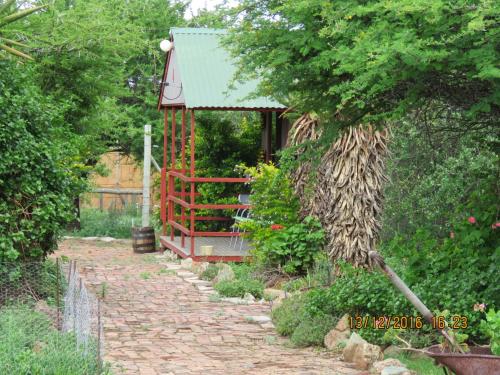 a brick path leading to a garden with a red gate at Klein Paradys Lodge - Polokwane in Polokwane
