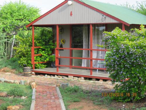 a red cottage with a porch and a dog in front at Klein Paradys Lodge - Polokwane in Polokwane