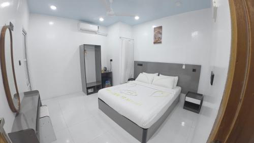 a white bedroom with a bed and a mirror at Skyinn omadhoo in Omadhoo