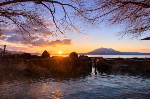 a sunset over the water with a mountain in the background at Sapporo's Secret Onsen Sanctuary Marukoma Onsen Ryokan in Chitose