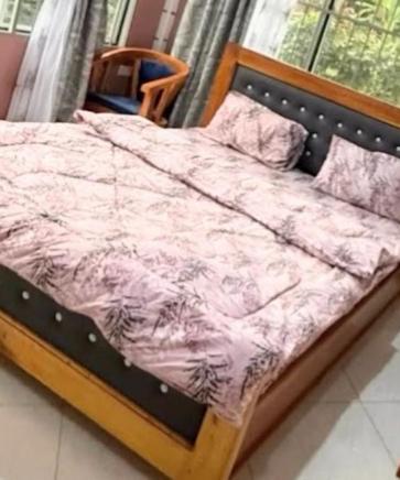 a bed with a pink comforter and a chair at Bibi Cosy Cottage in Moshi